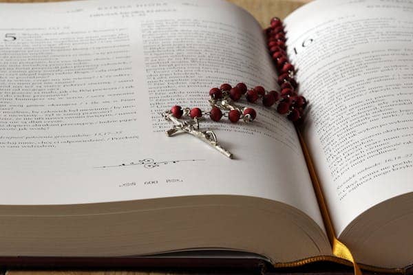 Biblia abierta con la camándula en el centro para aumentar la fe católica